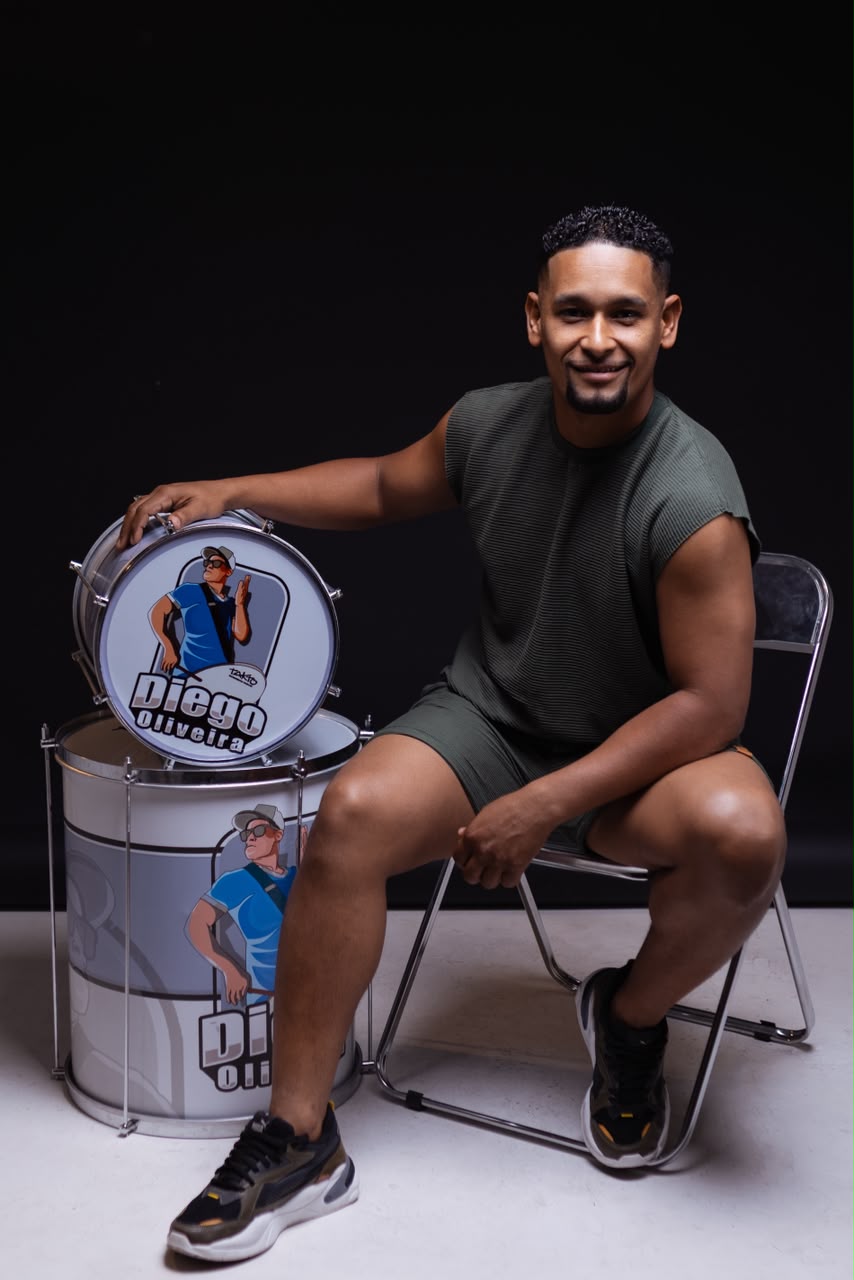 Diego Oliveira sentado ao lado de instrumentos de percussão com sua marca